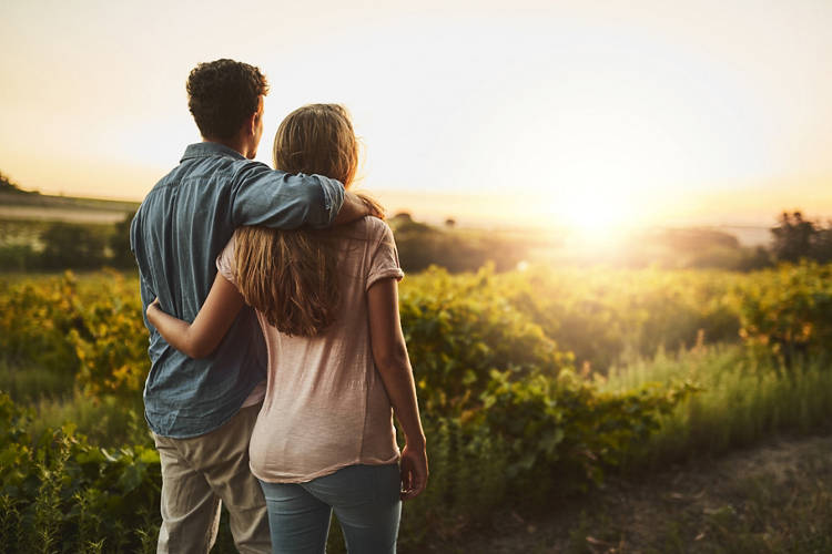 Shot of a young couple walking through their crops while holding each other and looking into the horizon