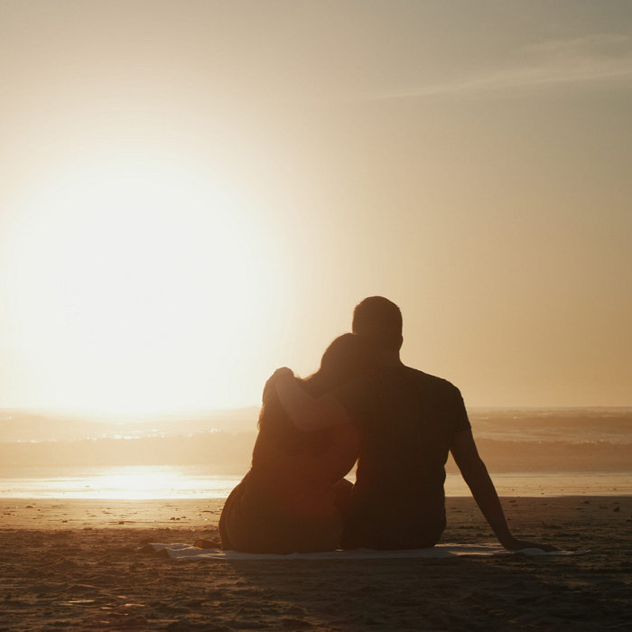 Couple, sunset and beach while on a romantic nature date watching ocean view on a picnic during their vacation. Love, travel and summer holidays with lovers in silhouette from behind for a honeymoon