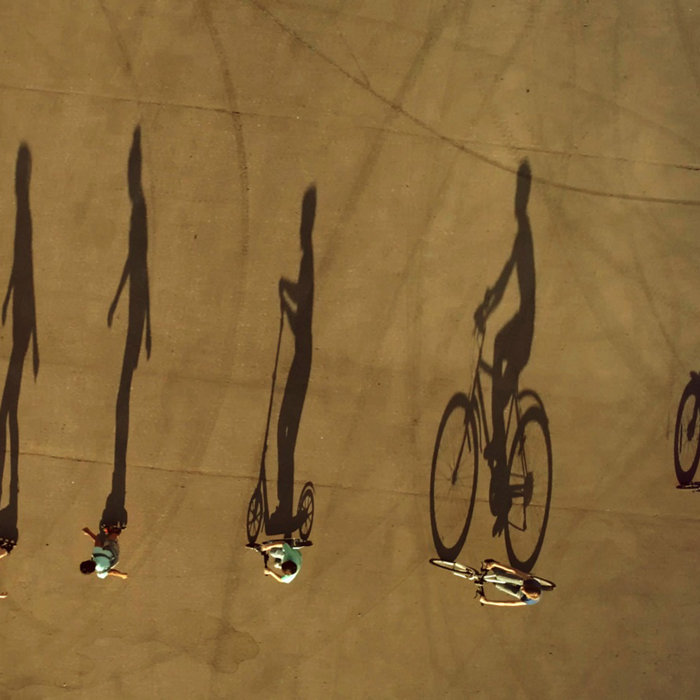 A group of preadolescents children dressed in a summer casual clothes are riding the eco alternative city transport (bikes, scooter, roller skates and self balancing scooter) at the walk on city square. Aerial top view, drone shot, outdoors in a summer at a sunset with large shadows