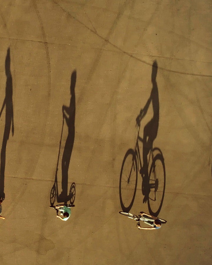 A group of preadolescents children dressed in a summer casual clothes are riding the eco alternative city transport (bikes, scooter, roller skates and self balancing scooter) at the walk on city square. Aerial top view, drone shot, outdoors in a summer at a sunset with large shadows