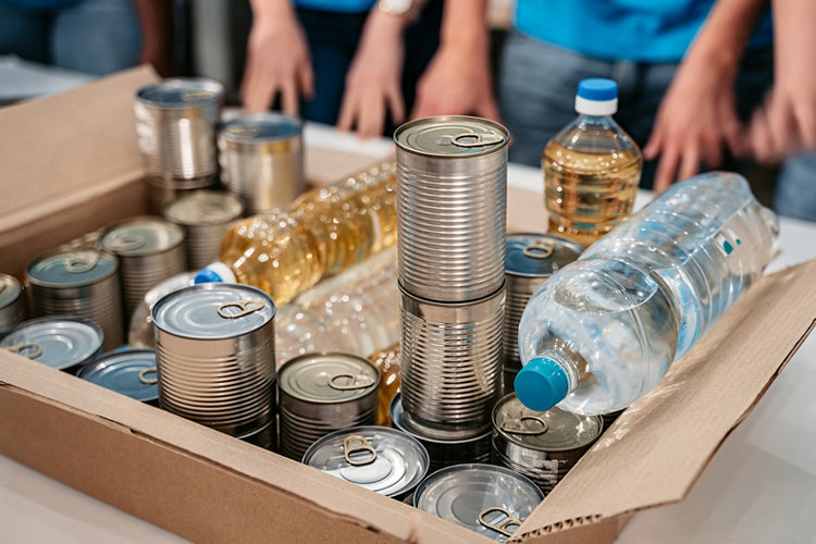 Box with with oil, canned food and water bottles for donations, close up.