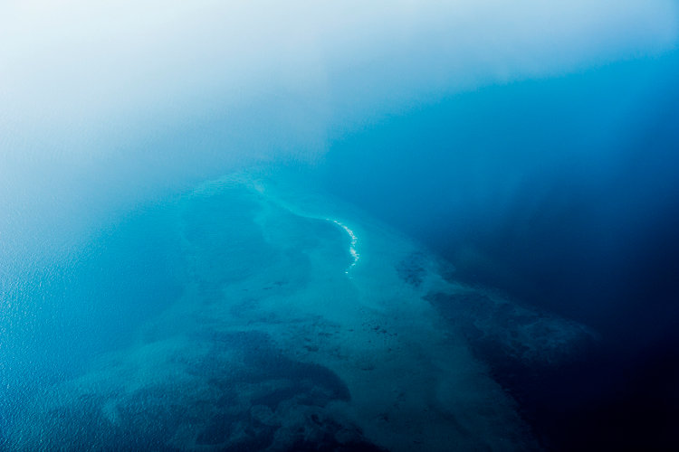 An aerial view of sea currents and a reef in the open ocean.