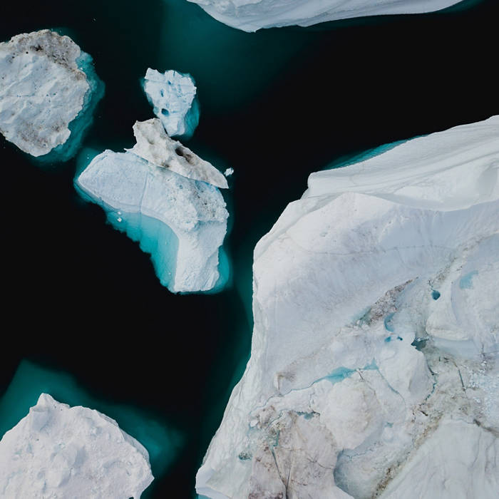 Aerial view of icebergs floating in dark water, showcasing contrasting white ice and deep blue sea in a polar region