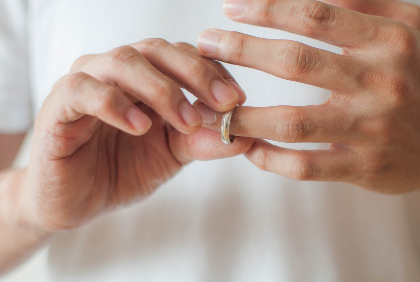 A close-up view of a young man's hands removing his wedding ring a concept of relationship difficulties